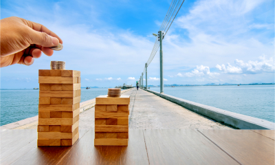 Hand of man puts money on the top of wooden blocks stacked on a bridge