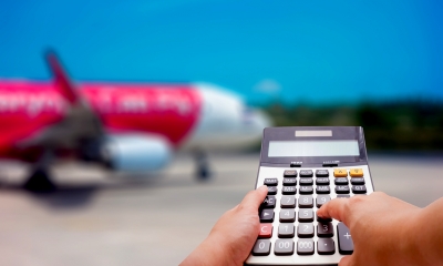 Person using a calculator in front of a plane before going on holiday