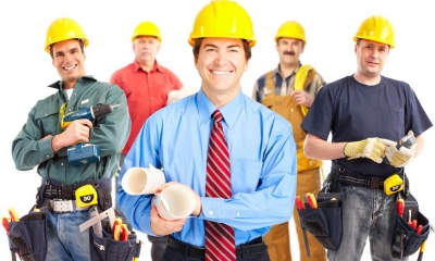 Group of construction workers in yellow hard hats holding various construction items