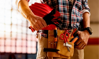 Closeup of bricklayer hands holding hardhat and construction equipment.