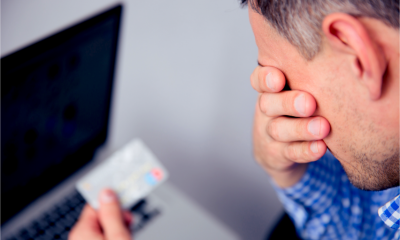 Upset man holding credit card with laptop on background as he struggles with debt