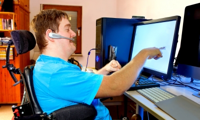 Disabled man in a special chair touching the computer screen at the workplace