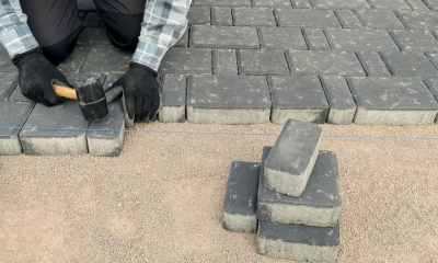 Person wearing gloves laying bricks on the floor to make a driveway or patio
