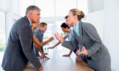 Employees wearing grey suits shouting at each other in a board meeting