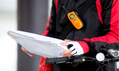 Man in a red and black jacket holding a parcel while on his bicycle