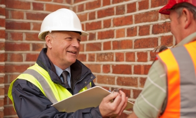 Health and safety Builder with white helmet and hi-viz jacket holding clipboard
