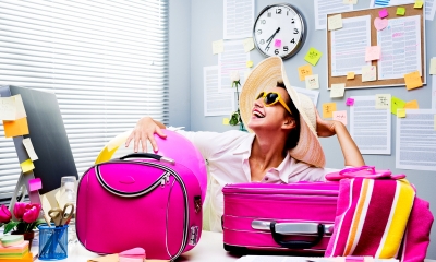 Woman wearing a beach hat and glasses with pink suitcases on her desk