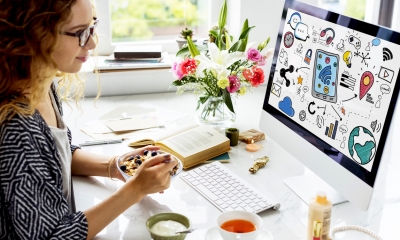 Woman sits in front of her computer eating breakfast