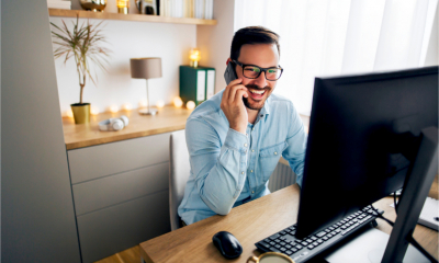 Smiling employee working remotely from home. He is speaking on the phone.