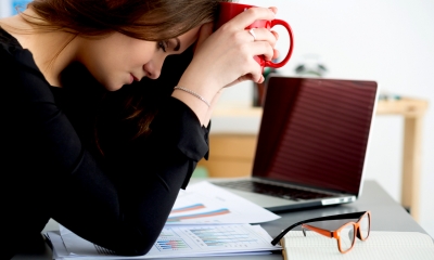 Woman upset at home office holding a red mug up to her head with both hands