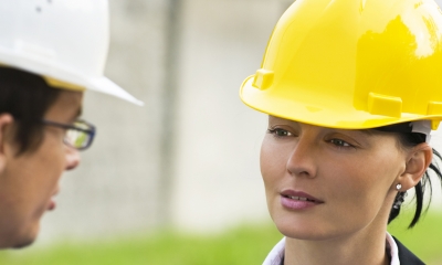 Managing health and safety Female worker wearing yellow hard had chats with male worker wearing white hard hat