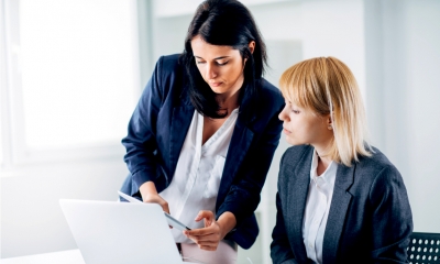 Female business executive explains something to another seated female business executive