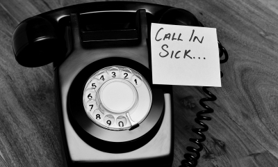 'CALL IN SICK' written on a post-it note on a telephone representing online absence