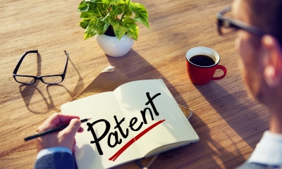 Patents Man sitting at desk with a cup of coffee writes Patent in an open notebook