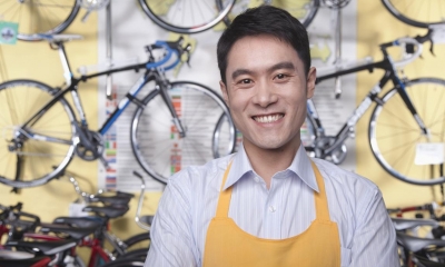 Man in shirt and yellow apron in front of multiple bicycles in bicycle shop