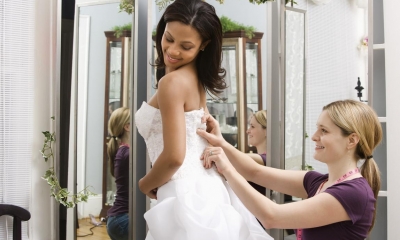 Woman fitting wedding dress onto bride in bridal shop