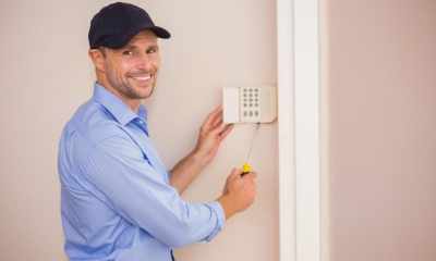 Man in blue shirt and cap fitting alarm onto a wall