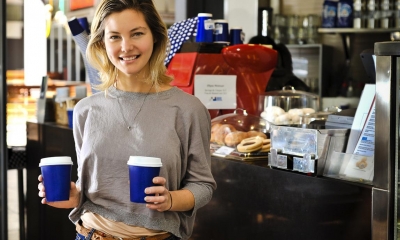 Woman holding two cardboard cups of coffee in front of till