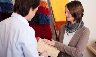 Woman feeling beige carpet sample from employee in carpet shop