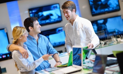 Man with arm around woman in computer shop being served by employee