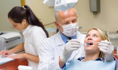 Male dentist treating a female patient with assistant in background