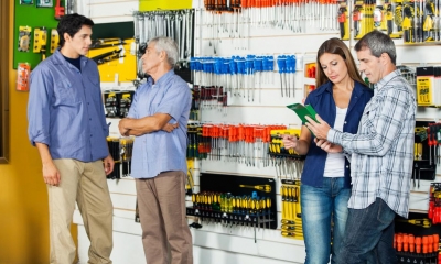 Two customers in DIY shop being served by employees with multiple tools in background