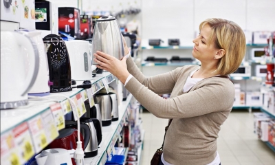 Woman holding kettle next to shelf of kettles in electrical shop
