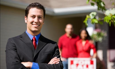 Man in suit with two customers in background in red tops with sold house