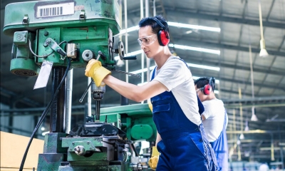 Man operating machinery in factory with another man in background using machinery