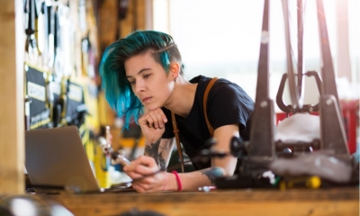 Female worker with blue hair looking for music on her laptop