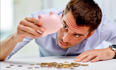 Man in a blue shirt looking into an empty piggy-bank with coins on the table