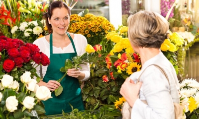 Florist surrounded by various types of flowers serving a customer