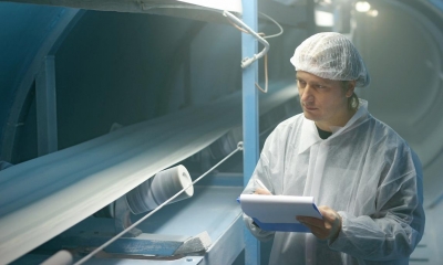 Man in work gear holding clipboard stood next to food conveyor belt