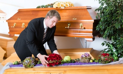 Man laying flowers in a brown coffin