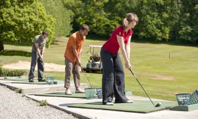 Multiple people playing golf at a driving range on a sunny day