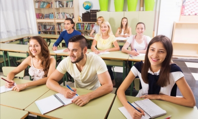 Multiple students in a classroom writing in their notepads