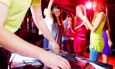 DJ using decks at party with people dancing in background