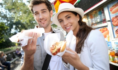 Man and woman eating hot dogs outside hotdog stand