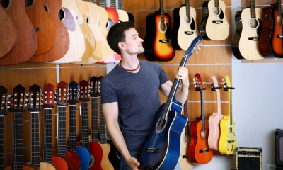 Man holding blue guitar with multiple guitars in background in music shop