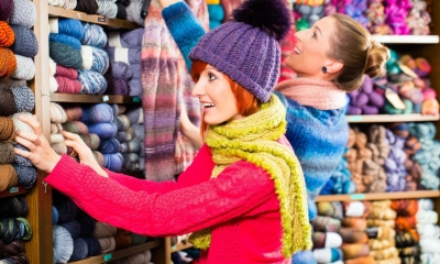 Woman in hat looking through various bundles of wool on shelf with woman in background