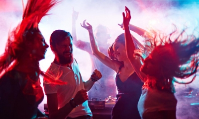 Multiple people dancing in dark nightclub with lights in the background
