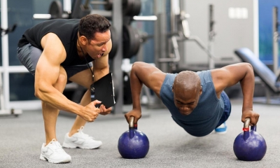 Personal trainer motivating client who is using barbells to do pushups