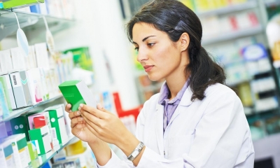 Pharmacist holding green medicine packet in pharmacy shop