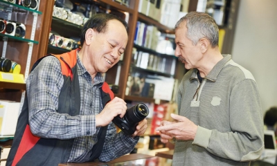 Man holding black camera with customer in background looking at photo equipment