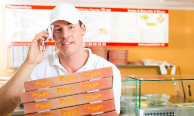 Man on phone holding stack of pizzas in pizza takeaway shop