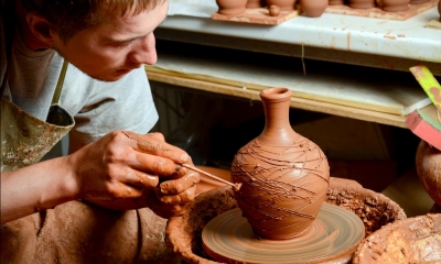 Man sitting down making vase out of brown clay using tool