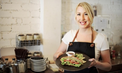 Woman holding plate with sandwich on it in sandwich bar