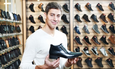 Man holding black shoe in shoe shop with multiple shoes in background