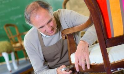 Man in grey jumper and brown dungarees repairing wooden chair