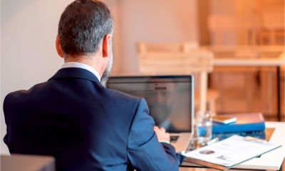 Bearded man in a suit sat down facing away from the camera using his laptop